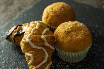 Set of pastries consisting of croissants and muffins on a dark background
