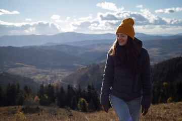 Young happy woman in orange beanie is walking in front of mountains landscape