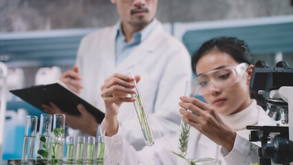 Researcher woman are looking to simple substance in tube on her hands researcher man are standing, looking and taking notes at cosmetic lab and laboratory