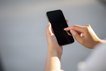 Portrait of a woman holding a smartphone with a blank copy area screen for your text message or content. A woman reading a message on her mobile phone while in town.