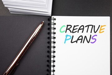 Words CREATIVE PLANS on a notepad with a pen.Search for creative ideas.