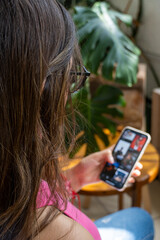 Happy millennial hispanic teen girl checking social media holding smartphone at home.