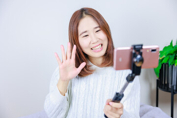 携帯電話のカメラに向かって笑顔で手を振る女性