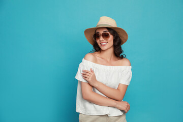 Fototapeta premium Beautiful young woman with straw hat and stylish sunglasses on light blue background