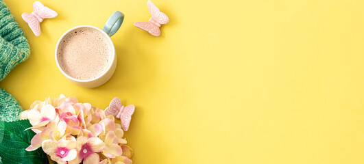 Cup of coffee, flowers and knitted element on yellow background, flat lay.