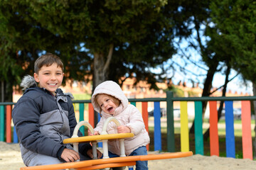 Fototapeta na wymiar Portrait of a girl and a boy sitting on a swing in a playground