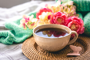 Home composition with a cup of tea, flowers and a knitted element in the bed.