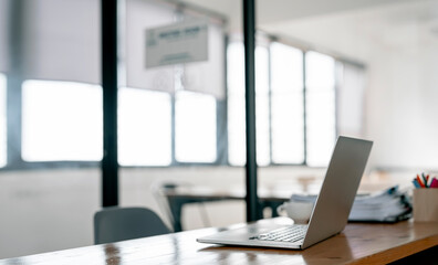 Creative workspace with laptop computer and document on wooden table in bright office room.