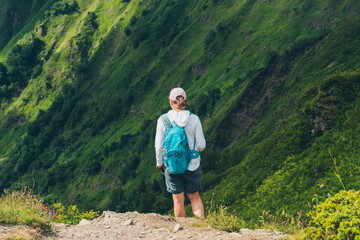 Naklejka na ściany i meble A female traveler with backpack on the top of a mountain. Mountain peaks. Krasnaya Polyana, Sochi, Russia. Climbing the mountain.