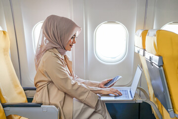 Asian muslim businesswoman working on digital laptop computer during the flight for her business...