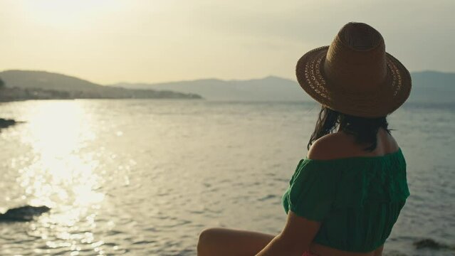 A girl in a hat takes a selfie at sunset by the sea. A beautiful woman on vacation edits and looks at the sun and takes a photo on the phone. High quality 4k footage