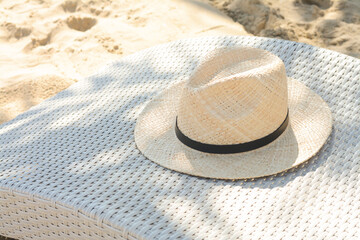 Fototapeta na wymiar Sunbed with stylish straw hat on sandy beach, space for text