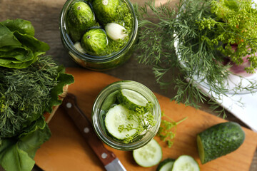 Glass jars, fresh cucumbers and herbs on wooden table, flat lay. Pickling recipe