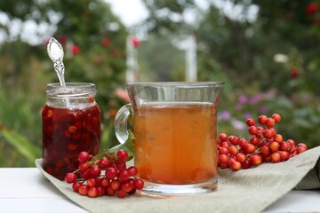 Cup of tea, jam and ripe viburnum berries on table outdoors