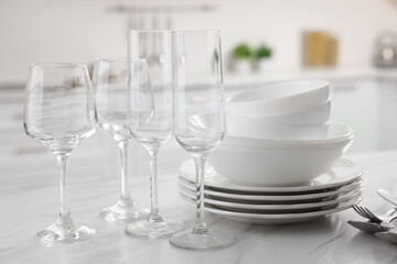 Different clean dishware, cutlery and glasses on white marble table in kitchen, closeup