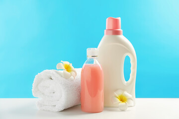 Obraz na płótnie Canvas Bottles of laundry detergents, towel and plumeria flowers on white table