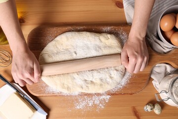 Woman rolling dough with wooden pin at table, top view