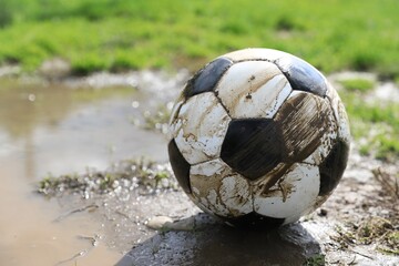 Dirty soccer ball on green grass near puddle outdoors, closeup. Space for text