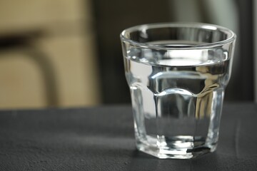 Glass of pure water on black table against blurred background, space for text