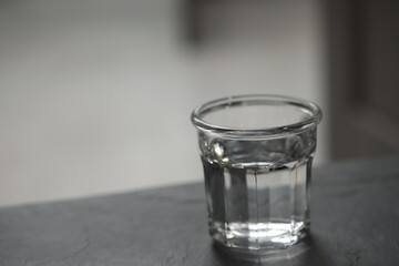 Glass of pure water on black table against blurred background, space for text