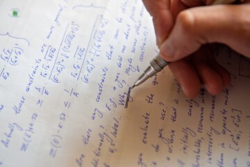 Student writing mathematical calculations on paper, closeup