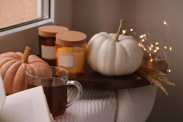 Beautiful pumpkins, tea and candles on window sill indoors
