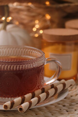Cup of hot drink with cookies on wicker mat indoors