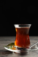 Glass with traditional Turkish tea on grey table against black background