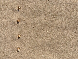 Fototapeta na wymiar Four cigarette butts arranged as bullet points in sand on beach