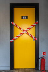 closed yellow door of the toilet for women and men sealed with fencing tape and a red fire extinguisher