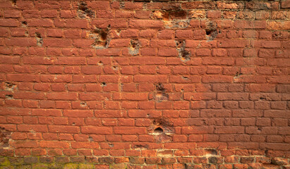 Shell marks on the red brick wall. The consequences of splinters hitting the wall of the building. Traces of shelling on the house.