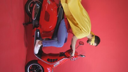 A young man plays the role of a superhero, he is dressed in a cloak and mask, a man is sitting on a scooter on an isolated background.