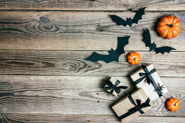 Gift boxes with black ribbons, pumpkins and paper bats on the old wooden boards.