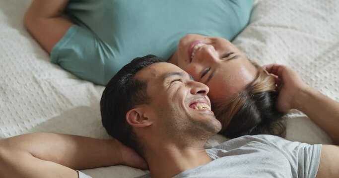 Happy couple, bedroom and talking while lying on bed for love and marriage bonding happiness in comfy home. Asian man and woman joke and relax in romantic hotel together in morning from above