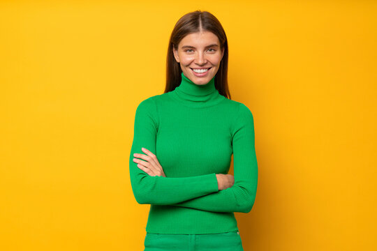Portrait of fashion designer in green turtleneck standing with crossed hands on yellow background