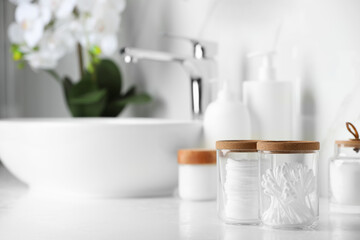 Glass jars with cotton pads and swabs on white countertop in bathroom. Space for text
