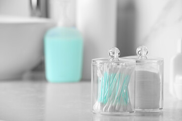 Containers with cotton swabs and pads on white countertop in bathroom. Space for text