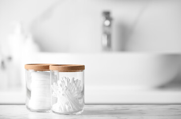 Glass jars with cotton pads and swabs on white countertop in bathroom. Space for text