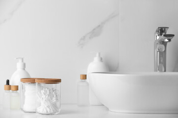 Fototapeta na wymiar Glass jars with cotton pads and swabs near cosmetic products on white countertop in bathroom