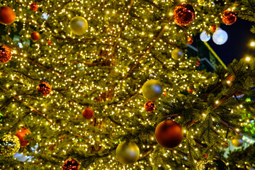 Obraz na płótnie Canvas Red and gold Christmas decorations hanging on the Christmas tree illuminated with lights