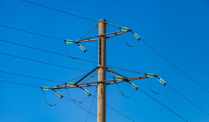 The upper part of a power line pole with insulators and wires against a blue sky background