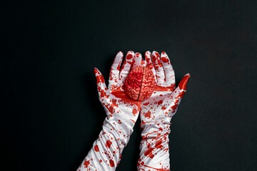 Creepy human brain in hands in bloody gloves on a black background. - obrazy, fototapety, plakaty