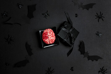 Creepy human brain in a gift box with Halloween decorations on a black background.