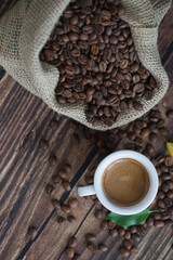 Cup of espresso near coffee beans and jute sack on wooden background