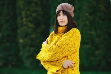 Beautiful European brunette dressed in a yellow woolen sweater and hat outside. The beautiful girl who wears thick stylish autumn clothes in cool weather.