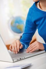 Female hand typing on laptop computer keyboard, globe in background.