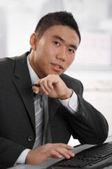 Confident young asian businessman sitting at desk looking at camera.