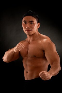 Young and muscular asian man in martial arts pose, studio shot against black background.