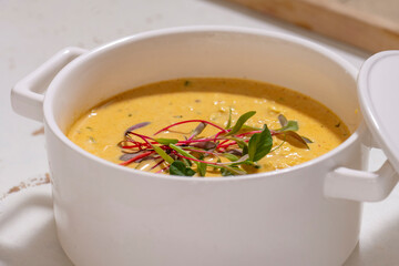 Pumpkin cream soup served with herbs in ceramic pot with lid