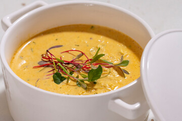 Pumpkin cream soup served with herbs in ceramic pot with lid